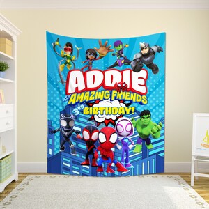 May include: A blue tapestry featuring cartoon characters and the text "Addie and his Amazing Friends 3rd Birthday!". The design includes illustrations of Spider-Man, Hulk, and other superheroes, set against a cityscape backdrop.