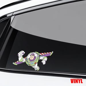 May include: A vinyl decal of Buzz Lightyear in a flying pose. The character is wearing a white, green, and purple spacesuit with red and white striped wings. The word "VINYL" is printed in red at the bottom right.