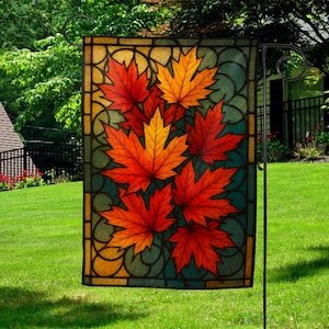 May include: A rectangular garden flag featuring a stained-glass design with vibrant red and orange maple leaves against a teal background. The flag is framed by a decorative border and displayed on a black metal stand, perfect for outdoor decor.