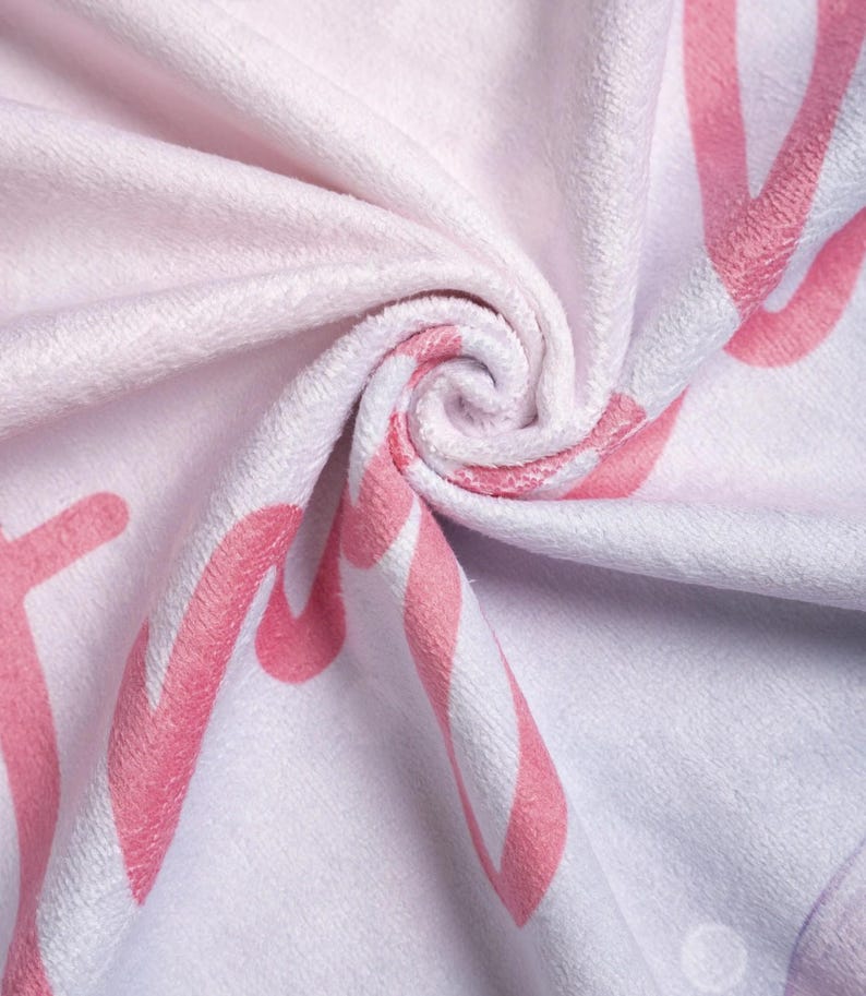 May include: A soft, folded pink and white towel with a swirling pattern. The towel features large, stylized pink lettering and a striped design. The overall color scheme is a light pink and white, creating a gentle and inviting aesthetic.