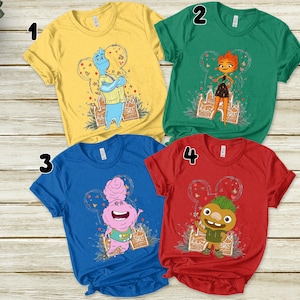 May include: Four short-sleeved t-shirts in yellow, green, blue, and red. Each shirt features a cartoon character design within a Mickey Mouse ear outline. The designs include a blue character, a fiery orange character, a pink character, and a green character.