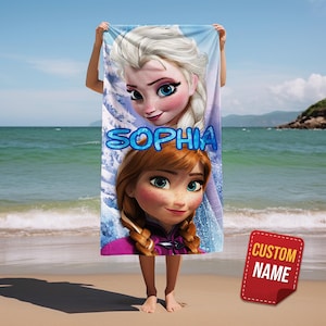 Pode incluir: Uma toalha de praia com Elsa e Anna de Frozen, com o nome "SOPHIA" em letras azuis de bolhas. A toalha &eacute; segurada em uma praia com o oceano ao fundo. Uma etiqueta vermelha com "CUSTOM NAME" est&aacute; no canto inferior direito.