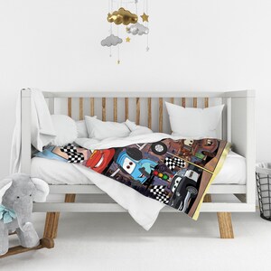 May include: A white baby blanket featuring a colorful graphic print of various cartoon race cars, including red, blue, and black vehicles, along with checkered flags and traffic light motifs, draped over the side of a white wooden crib.