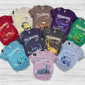 May include: A collection of ten short-sleeved t-shirts in various colors, each featuring a character from the movie Cars with their name, the year 2006, and a checkered flag graphic. The shirts are numbered one through ten and display characters including Lightning McQueen, Luigi, Tow Mater, Ramone, Chick Hicks, Finn McMissile, Doc Hudson, Cruz Ramirez, Sally Carrera, and Jackson Storm.