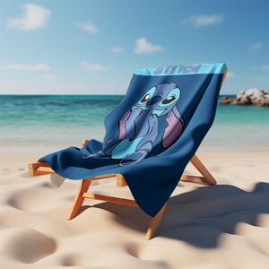 May include: A dark blue beach towel featuring a graphic illustration of the character Stitch with large ears and a wide smile. The word STITCH is printed in light blue block letters at the top of the towel, which is draped over a wooden beach chair.