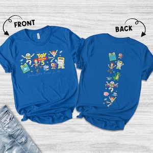 May include: A royal blue short-sleeved t-shirt featuring Toy Story 5 graphics. The front displays characters with the text "Toy Story 5" and "You've Got A Friend In Me." The back shows a vertical arrangement of various Toy Story character illustrations.