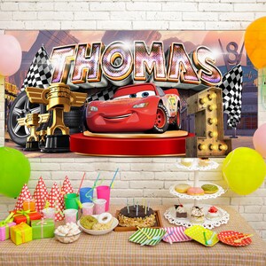 May include: A birthday party scene with a banner featuring the name "THOMAS" and a cartoon race car. Decorations include balloons, a cake, gifts, and a number "1" made of lights. The table is set with party supplies.