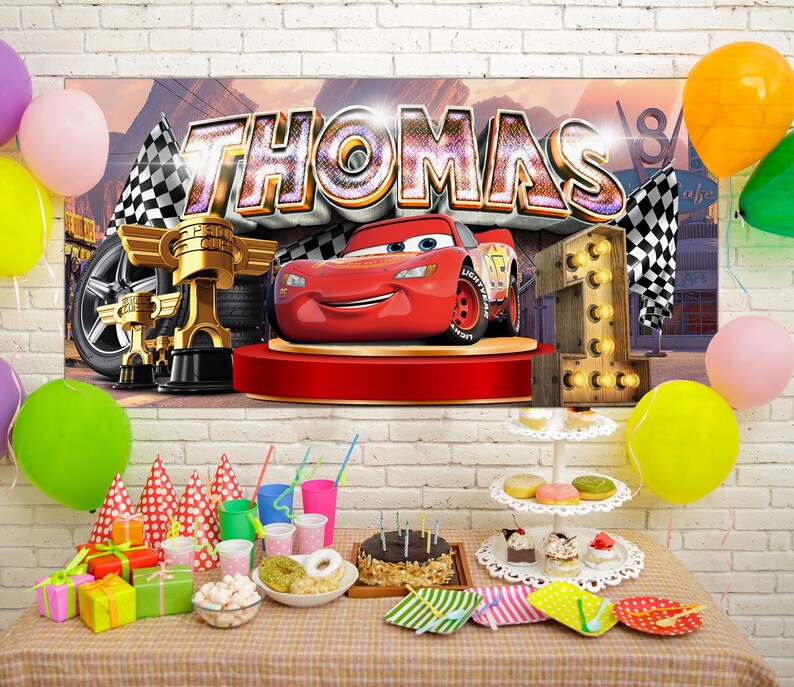 May include: A birthday party scene with a banner featuring the name "THOMAS" and a cartoon race car. Decorations include balloons, a cake, gifts, and a number "1" made of lights. The table is set with party supplies.