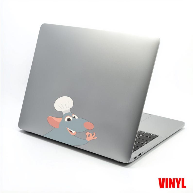 Puede incluir: Un port&aacute;til gris con una pegatina de un rat&oacute;n de dibujos animados con un gorro de chef en la tapa. El rat&oacute;n es azul con un gorro de chef blanco y una nariz y orejas rosas. La palabra "VINYL" est&aacute; impresa en rojo en la esquina inferior derecha.