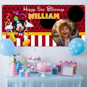 Może przedstawiać: Scena przyjęcia urodzinowego z banerem z Myszka Miki i napisem "Happy 5th Birthday WILLIAM". Baner ma czerwone tło w kropki. St&oacute;ł jest nakryty ciastem, babeczkami, balonami i czapeczkami.