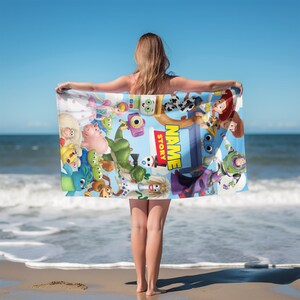 May include: A rectangular beach towel featuring a vibrant collage of animated characters from the Toy Story franchise, including Buzz Lightyear, Woody, and Jessie. The center displays the text NAME STORY in bold yellow letters on a blue background.