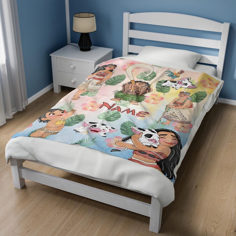 Puede incluir: Una colorida manta con personajes de dibujos animados y la palabra "NAME". El dise&ntilde;o incluye ilustraciones de personas, animales y flores tropicales. La manta est&aacute; extendida sobre una cama blanca.