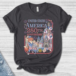 Puede incluir: Camiseta gris oscuro con un gr&aacute;fico colorido que celebra el 250 aniversario de los Estados Unidos de Am&eacute;rica. El dise&ntilde;o incluye personajes de dibujos animados, un castillo, fuegos artificiales y el texto "United States of America 250th Anniversary."