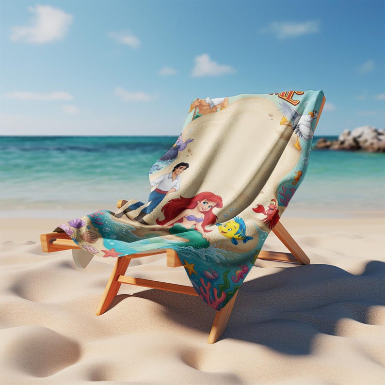 May include: A beach chair with a vibrant towel depicting characters from "The Little Mermaid." The towel showcases Ariel, Prince Eric, Flounder, and Sebastian on a sandy backdrop with ocean waves. The chair is constructed from light-toned wood and is positioned on a sandy beach.