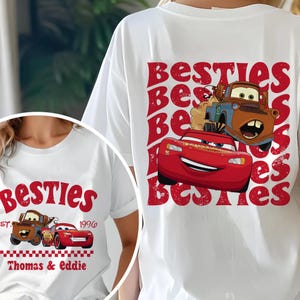 Może przedstawiać: Białe koszulki z czerwonym nadrukiem słowa "Besties" i samochodami z kresk&oacute;wek. Jedna koszulka przedstawia Zygzaka McQueena i Złomka, a druga napis "Thomas & Eddie" i rok 1996.