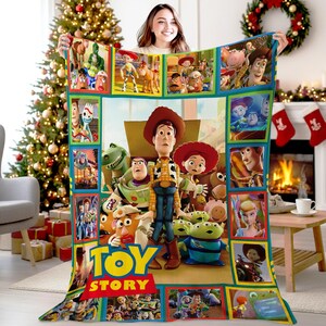 May include: A rectangular fleece blanket featuring a large central graphic of Woody, Buzz Lightyear, Jessie, and other Toy Story characters, surrounded by a border of smaller movie scene panels and the yellow and red Toy Story logo at the bottom.