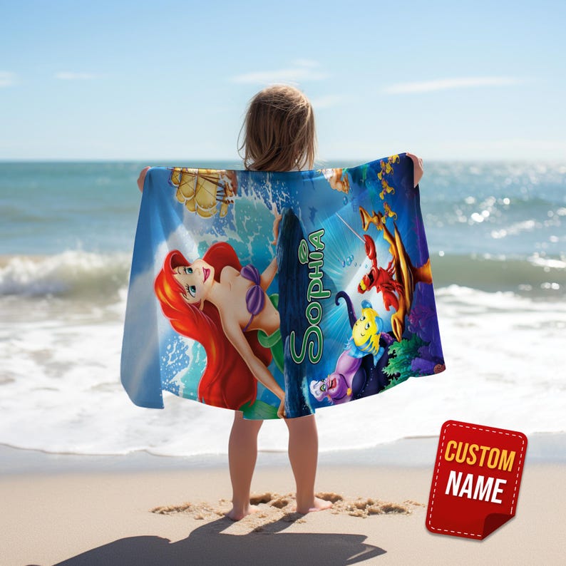 May include: A blue beach towel featuring Ariel from The Little Mermaid, with the name "Sophia" in green script. The towel has a vibrant design with ocean waves and cartoon characters. A red tag with "CUSTOM NAME" is in the lower right corner.