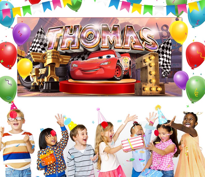 May include: A birthday banner featuring the name "THOMAS" in large, metallic letters, with a red race car and the number "1". The banner is decorated with balloons and checkered flags, suggesting a car-themed first birthday party.