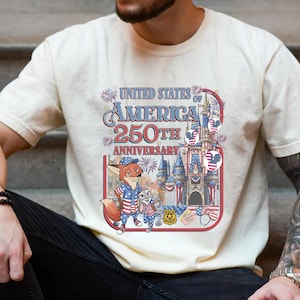 Puede incluir: Camiseta color crema con un gr&aacute;fico colorido que celebra el 250 aniversario de los Estados Unidos de Am&eacute;rica. El dise&ntilde;o incluye personajes de dibujos animados, un castillo y elementos patri&oacute;ticos en rojo, blanco y azul.