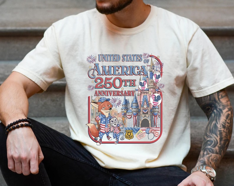Puede incluir: Camiseta color crema con un gr&aacute;fico colorido que celebra el 250 aniversario de los Estados Unidos de Am&eacute;rica. El dise&ntilde;o incluye personajes de dibujos animados, un castillo y elementos patri&oacute;ticos en rojo, blanco y azul.