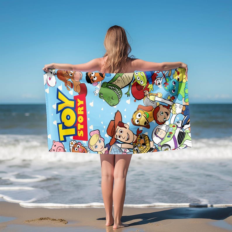 May include: A blue beach towel featuring characters from the animated film "Toy Story." The towel has the words "Toy Story" in large, colorful letters. The towel is decorated with images of Woody, Buzz Lightyear, and other characters from the movie.