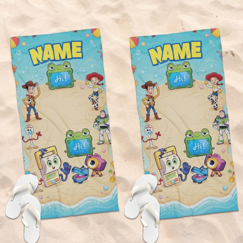 May include: Two beach towels with a cartoon beach scene featuring characters. The towels have a blue border with the word "NAME" in yellow. The beach scene includes cartoon characters, a frog with "Hi!" on a sign, and white flip-flops.