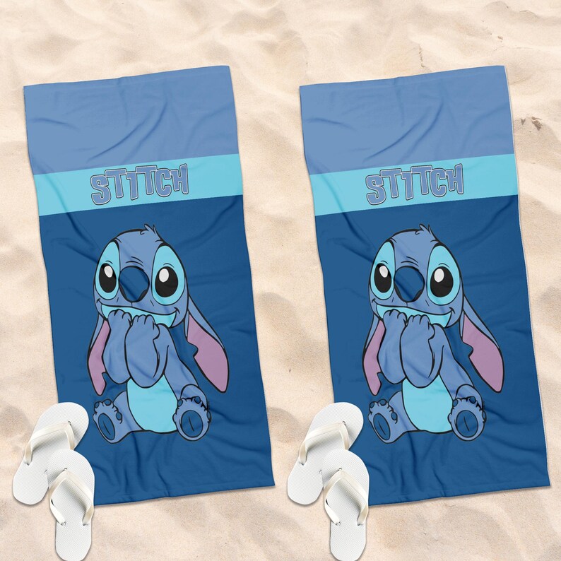 May include: Two rectangular blue beach towels featuring a graphic of the character Stitch with the text STITCH printed in light blue. Each towel is paired with a pair of white flip-flops, displaying a consistent design across both items.