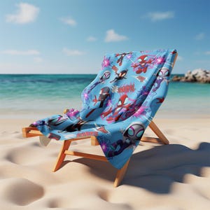 Puede incluir: Una toalla de playa azul claro con un patr&oacute;n repetitivo de superh&eacute;roes de dibujos animados en trajes rojos, negros y blancos, telara&ntilde;as y gr&aacute;ficos de estrellas rosas, colocada sobre una silla de playa de madera.