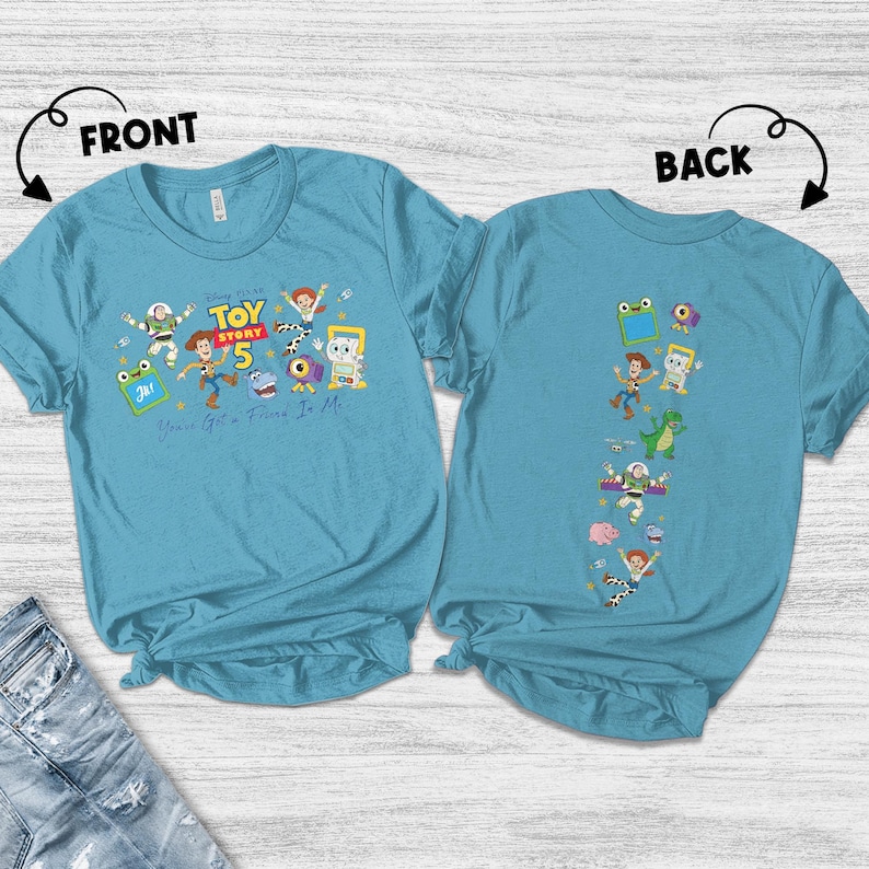 May include: A teal short-sleeve t-shirt shown from the front and back. The front features Toy Story 5 graphics with characters and the text You've Got A Friend In Me. The back displays a vertical column of various Toy Story character illustrations.