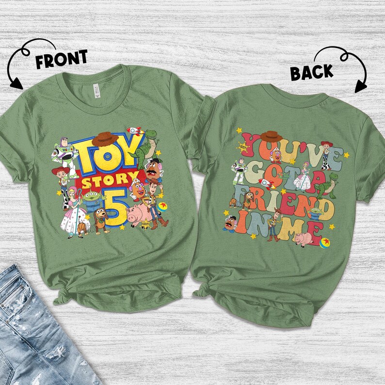 K&ouml;nnte beinhalten: Zwei olivgr&uuml;ne T-Shirts mit den Aufdrucken "Toy Story 5" und "You've Got a Friend in Me". Das vordere Shirt zeigt verschiedene Toy Story-Charaktere. Das hintere Shirt hat die gleichen Charaktere und den gleichen Text.
