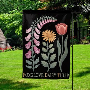 May include: Black garden flag featuring floral illustrations of foxglove, daisy, and tulip. The foxglove is pink, the daisy is yellow, and the tulip is peach. The words "FOXGLOVE DAISY TULIP" are printed at the bottom of the flag.