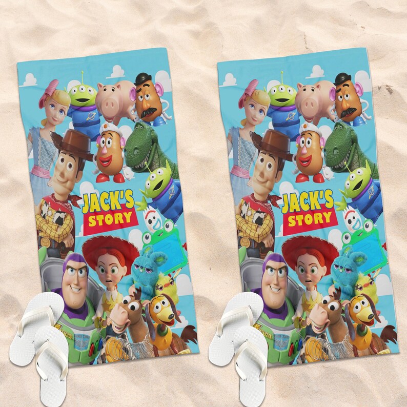 Peut inclure: Deux serviettes de plage bleues avec des personnages du film "Toy Story". Les serviettes ont un fond bleu clair avec des images de Woody, Buzz l'&Eacute;clair et d'autres personnages. Des tongs blanches sont au premier plan.