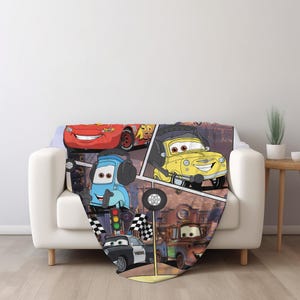 May include: A soft throw blanket featuring a colorful graphic print of various animated car characters from the movie Cars, including a red race car, a yellow car with headphones, a blue car, a black and white police car, and a brown tow truck.