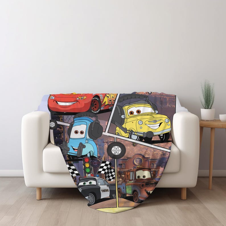May include: A soft throw blanket featuring a colorful graphic print of various animated car characters from the movie Cars, including a red race car, a yellow car with headphones, a blue car, a black and white police car, and a brown tow truck.