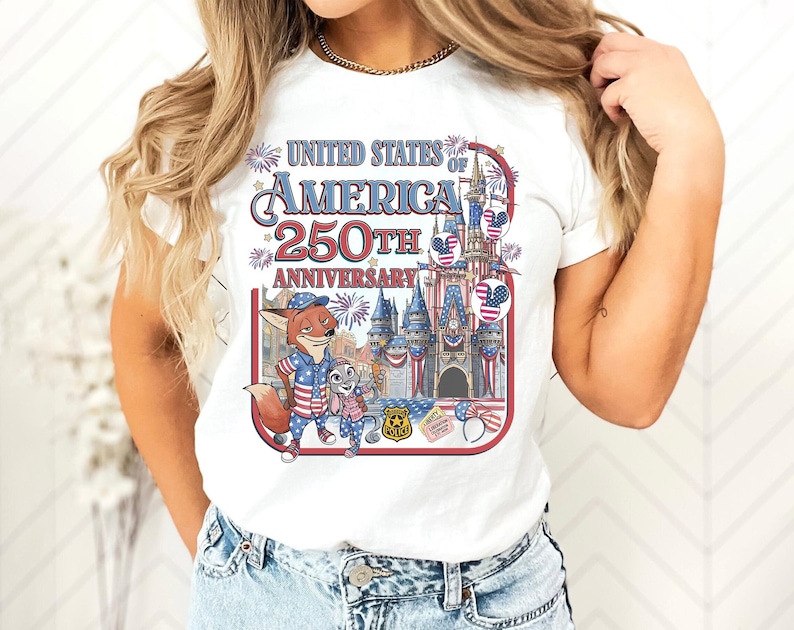 Puede incluir: Camiseta blanca con un gr&aacute;fico colorido que celebra el 250 aniversario de los Estados Unidos de Am&eacute;rica. El dise&ntilde;o incluye personajes de dibujos animados, un castillo, fuegos artificiales y el texto "UNITED STATES OF AMERICA 250TH ANNIVERSARY".