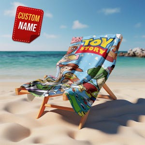 May include: A wooden beach chair with a blue Toy Story-themed towel draped over it. The towel features various characters from the movie and the words "Toy Story" in yellow and red. A red tag with the words "CUSTOM NAME" is in the upper left corner.