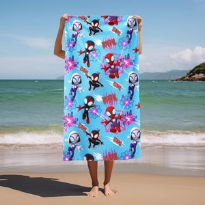 Puede incluir: Una toalla de playa rectangular de color azul claro con un patr&oacute;n repetitivo de superh&eacute;roes de dibujos animados en trajes rojos, negros y blancos, telara&ntilde;as rosas y el nombre DAVIL impreso en letras rojas. La toalla muestra varias poses.