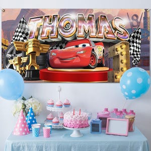 May include: A birthday party scene with a banner featuring the name "THOMAS" and a red race car. The table is set with a cake, cupcakes, party hats, balloons, and other decorations. A blue tablecloth completes the festive look.