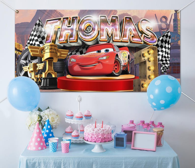 May include: A birthday party scene with a banner featuring the name "THOMAS" and a red race car. The table is set with a cake, cupcakes, party hats, balloons, and other decorations. A blue tablecloth completes the festive look.