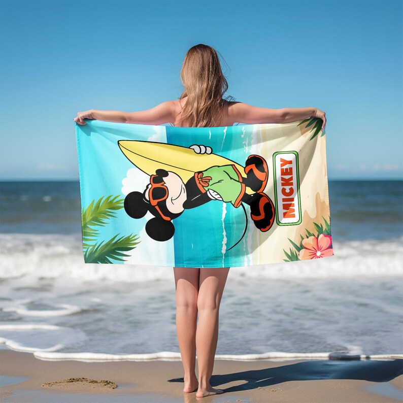 K&ouml;nnte beinhalten: Ein rechteckiges Strandtuch mit einer Cartoon-Illustration von Mickey Mouse, der eine orangefarbene Sonnenbrille und eine gr&uuml;ne Shorts tr&auml;gt und ein gelbes Surfbrett h&auml;lt. Der Hintergrund zeigt einen Strand mit Palmen und dem Text MICKEY.