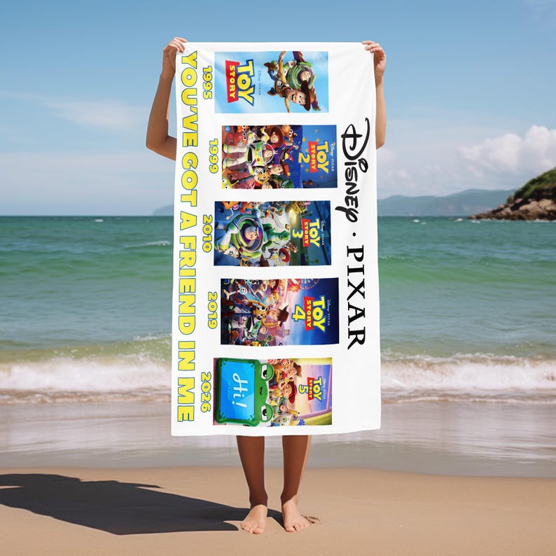 May include: A white rectangular beach towel featuring five stacked Toy Story movie posters from 1995, 1999, 2010, 2019, and 2026. The text YOU'VE GOT A FRIEND IN ME is printed vertically in yellow, with the Disney Pixar logo in black on the right.