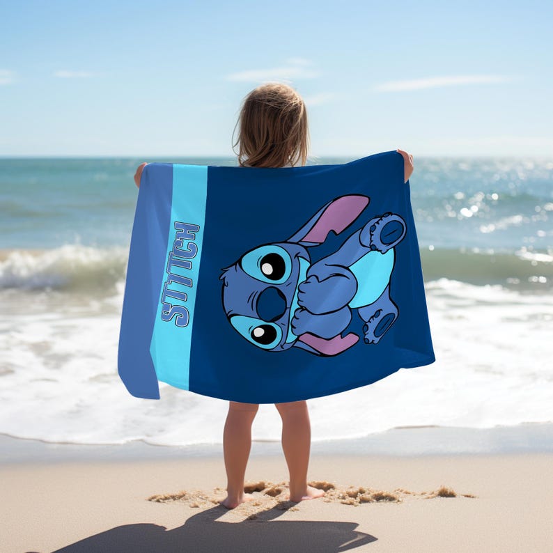 May include: A rectangular beach towel featuring a dark blue background with a large graphic of the character Stitch. The towel includes a light blue vertical stripe on the left side with the word STITCH printed in a bold, blue, outlined font.