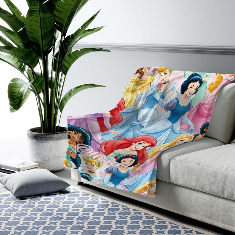 Pu&ograve; includere: Una morbida coperta con un colorato motivo ripetuto di varie principesse Disney, tra cui Cenerentola, Biancaneve, Ariel e Jasmine, con la parola Disney stampata in corsivo sulla superficie del tessuto.