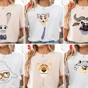 May include: A collection of six short-sleeved crew neck t-shirts in white and beige, each featuring a different cartoon animal character graphic on the front, including a rabbit, a fox with a tie, a buffalo, a sheep with glasses, a lion, and a leopard.