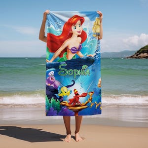 May include: A beach towel featuring a colorful illustration of Ariel from The Little Mermaid, with the name "Sophia" in green script. The design includes other characters from the movie, set against a blue ocean background.