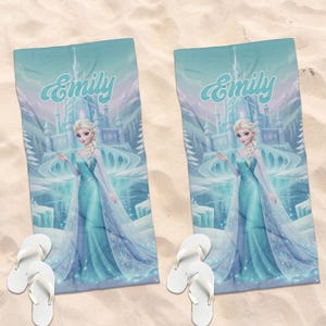May include: Two rectangular beach towels featuring a printed illustration of a blonde character in a light blue gown standing before an ice castle, with the name Emily written in script above. Each towel is paired with a pair of white flip-flops.