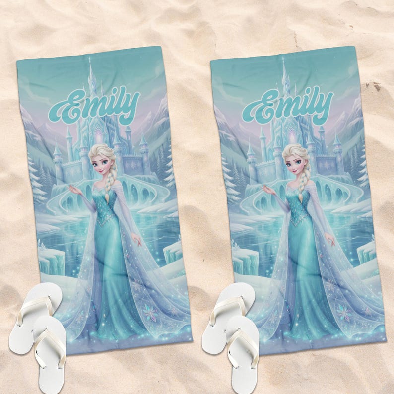 May include: Two rectangular beach towels featuring a printed illustration of a blonde character in a light blue gown standing before an ice castle, with the name Emily written in script above. Each towel is paired with a pair of white flip-flops.