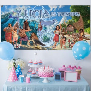 Puede incluir: Una escena de fiesta de cumplea&ntilde;os con una pancarta con personajes de una popular pel&iacute;cula de animaci&oacute;n. La pancarta dice "Lucia cumple 5". Hay globos azul claro y de lunares. Una tarta, cupcakes y art&iacute;culos de fiesta est&aacute;n sobre una mesa.