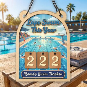 May include: Wooden swim tracker with the text "Laps Swum This Year" above a pool scene. The tracker displays "222" laps. The bottom of the tracker reads "Rome's Swim Tracker". The tracker is hanging by a chain.