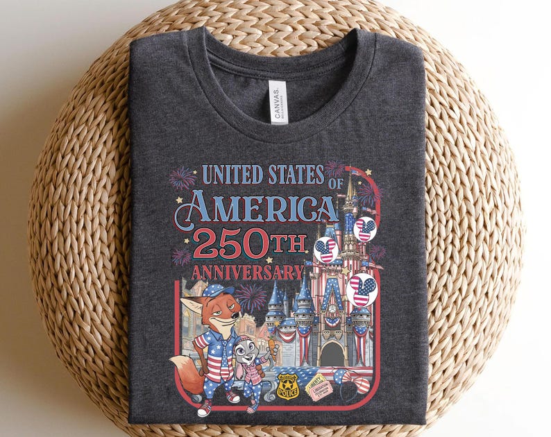 Puede incluir: Camiseta gris oscuro con un gr&aacute;fico colorido que celebra el 250 aniversario de los Estados Unidos de Am&eacute;rica. El dise&ntilde;o incluye fuegos artificiales, un castillo y personajes de dibujos animados. El texto "UNITED STATES OF AMERICA 250TH ANNIVERSARY" es visible.